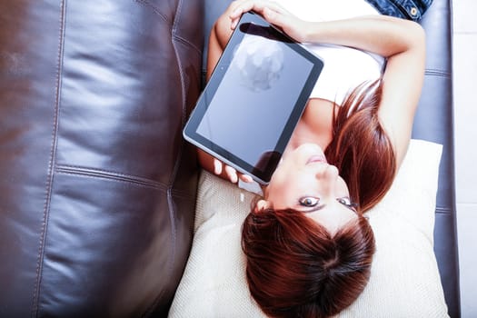 A young woman showing a Tablet PC while laying on the sofa.