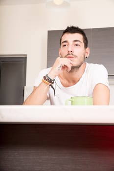 A young man sitting in the kitchen and drinking coffee.