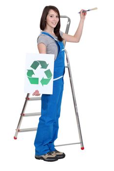 lovely brunet painter in blue dungarees holding brush and recycling logo