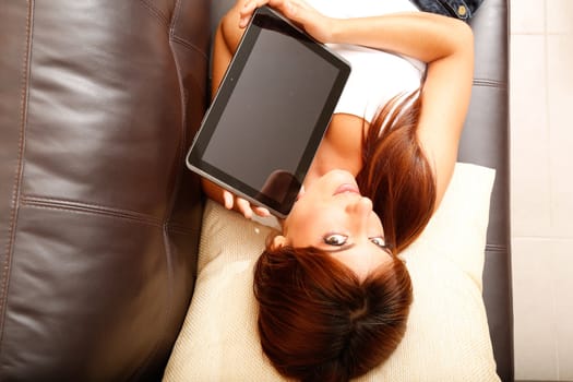 A young woman showing a Tablet PC while laying on the sofa.