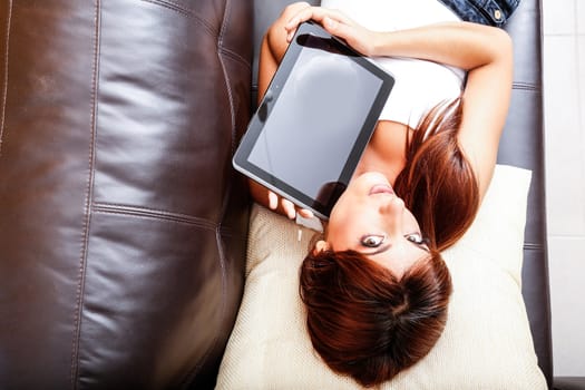 A young woman showing a Tablet PC while laying on the sofa.