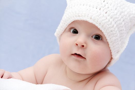 baby in white hat lies on bed