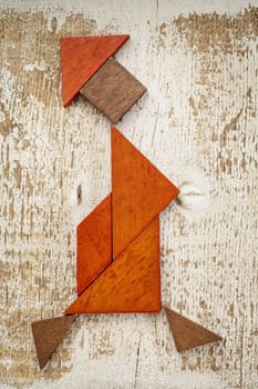 abstract figure of a walking woman built from seven tangram wooden pieces, a traditional Chinese puzzle game; rough white painted barn wood background