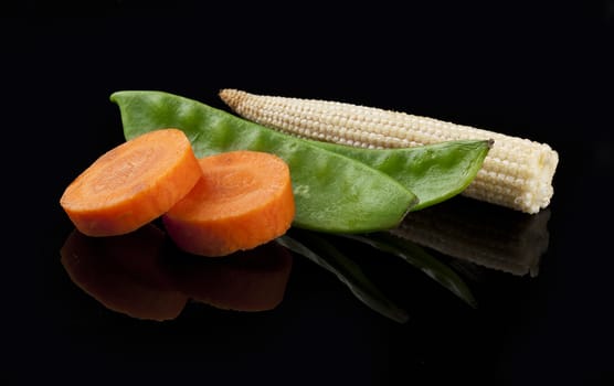 Fresh carrot, green peas and mini corn on the black background