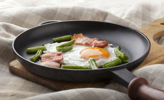 Fried egg with bacon and string bean on the black pan