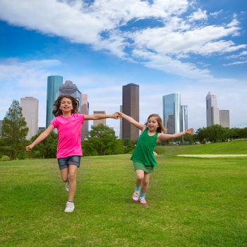 Two sister girls friends running holding hand in urban modern skyline on grass lawn