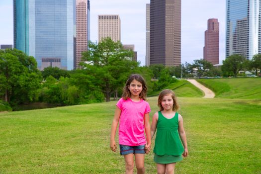 Two sister girls friends walking holding hand in urban modern skyline on grass lawn