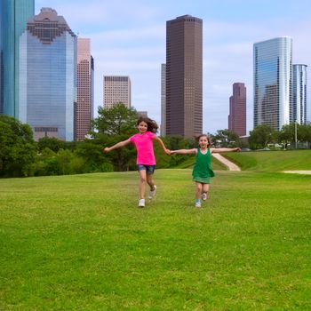 Two sister girls friends running holding hand in urban modern skyline on grass lawn