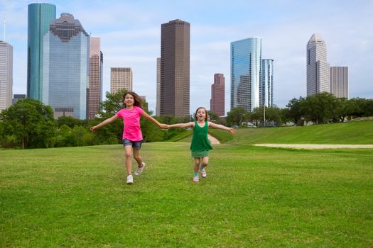 Two sister girls friends running holding hand in urban modern skyline on grass lawn