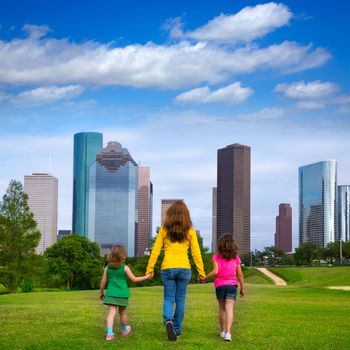 Mother and daughters walking holding hands on modern city skyline over park green lawn