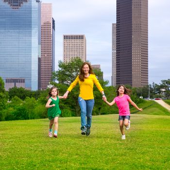 Mother and daughters walking holding hands on modern city skyline over park green lawn