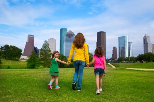 Mother and daughters walking holding hands on modern city skyline over park green lawn