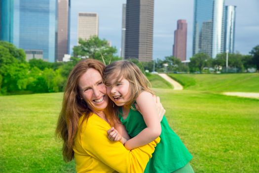 Mother and daughter happy hug laughing in park at city modern skyline background