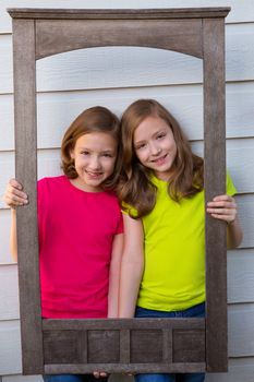 Twin sister girls posing with aged wooden border frame on white wall