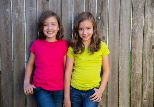 Twin sisters with different hairstyle posing on wood backyard fence