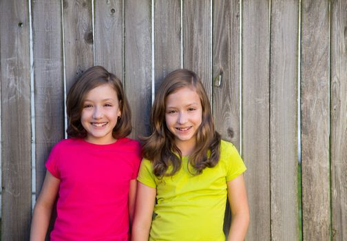 Twin sisters with different hairstyle posing on wood backyard fence