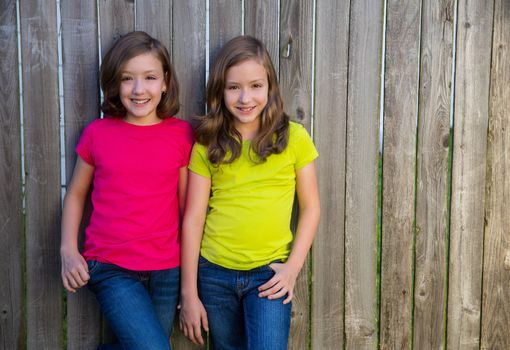 Twin sister girls with different hairstyle posing on wood backyard fence