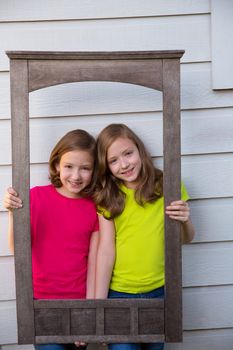 Twin sister girls posing with aged wooden border frame on white wall