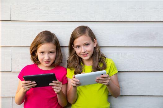 Twin sister girls playing with tablet pc happy on white wall looking camera