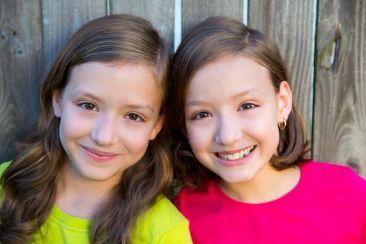 Happy twin sisters with different hairstyle smiling on wood backyard fence