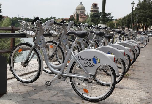 Verona, Italy - July 18, 2013: A row of public city bicycles, at the bank of River Adige in Verona, northern Italy, with Roman Catholic church San Giorgio in Braida visible in the background.