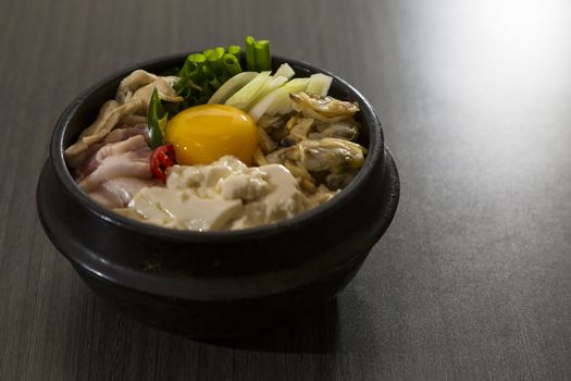 A heated stone bowl dish of korean food with raw eggs and seafood.