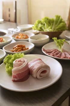 A vertical shot of sliced pork belly with korean side dishes.