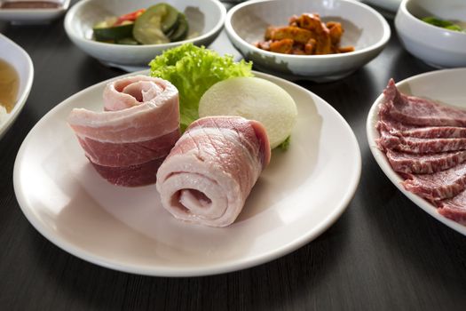 A horizontal shot of sliced pork belly with korean side dishes.