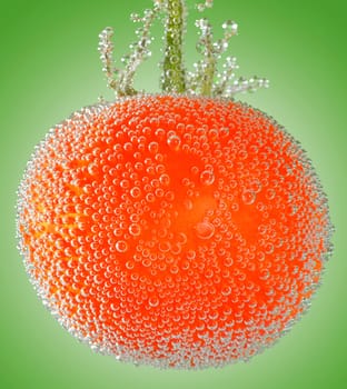 A fresh organic tomato immersed in mineral water on green background