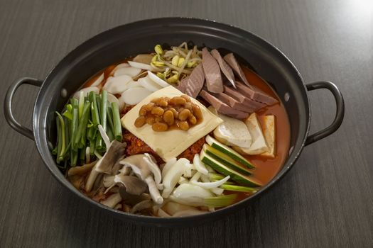 A heated wok of korean food with sliced ham, sausages and vermicelli- Budae Jeongol