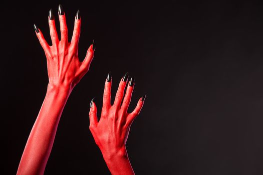 Red devil hands with black nails, Halloween theme, studio shot on black background 