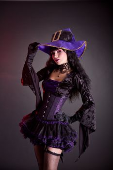 Cheerful witch in purple and black gothic fantasy Halloween costume, studio shot on black background 