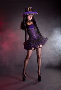 Sexy witch in purple and black gothic fantasy Halloween costume, full length shot  