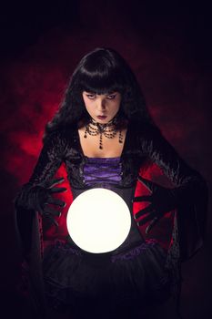 Beautiful witch or fortune teller with a crystal ball, studio shot over smoky background 