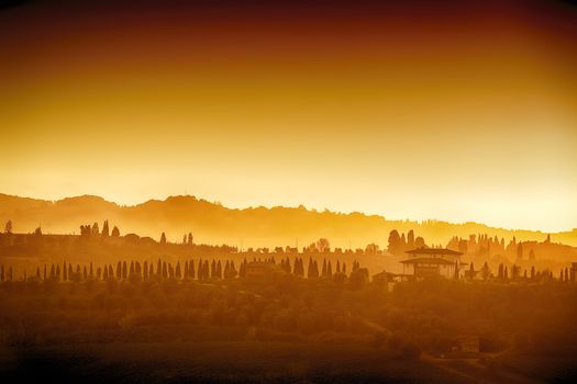 Landscape of Tuscany with hills, cypresses and houses at sunset