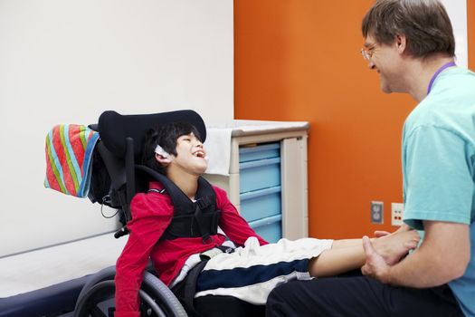 Disabled boy in wheelchair sharing laugh with his doctor or therapist