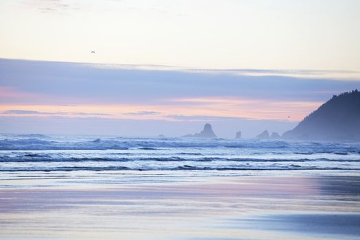 Colorful pastel hues in sky over Cannon Beach, Oregon with waves crashing on waves
