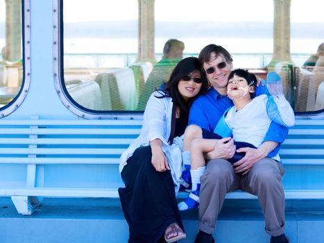 Smiling multiracial, interracial couple holding disabled son on ferry boat deck. Child has cerebral palsy.