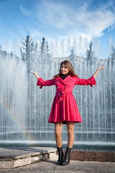 happy woman in a red cloak with his hands up at the fountain