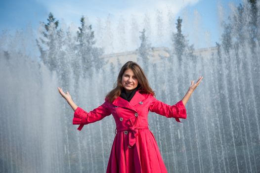 happy woman in a red cloak with his hands up at the fountain