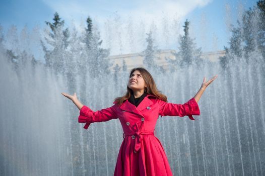 happy woman in a red cloak with his hands up at the fountain