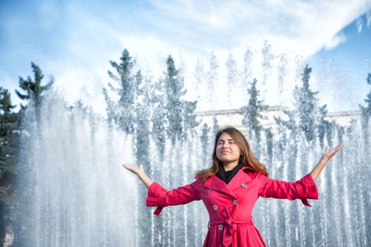 happy woman in a red cloak with his hands up at the fountain