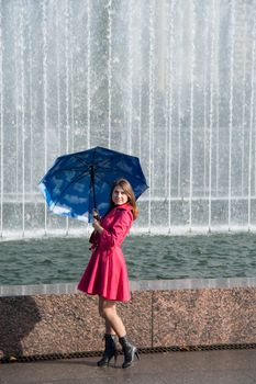 happy young woman in a red raincoat with an umbrella
