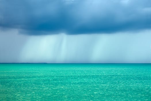 Storm rain clouds over the sea with a turquoise surface illuminated by the sun