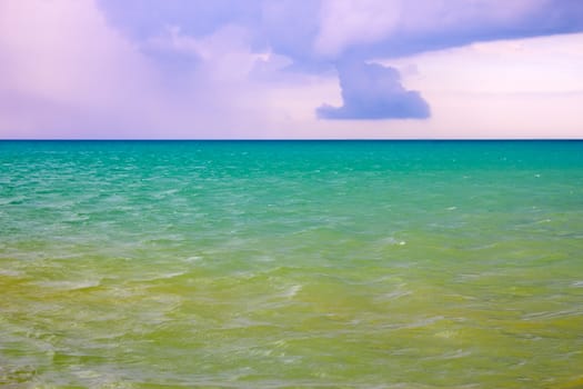 Thick cumulonimbus clouds over the sea with a turquoise and yellowish surface illuminated by the sun