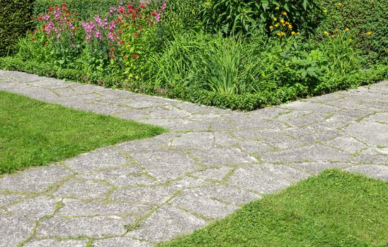 Stone paths crossing in a summer garden full of blooming flowers.