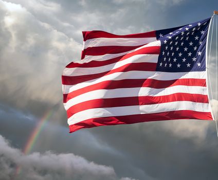American flag waving against a cloudy sky with a rainbow