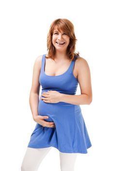 Cheerful pregnant redhead woman smiling at camera, touching her belly on white