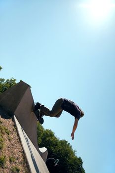 Silhouette of a young skateboarder doing a wall ride trick at the top of the ramp at a concrete skate park. Slight lens flare.