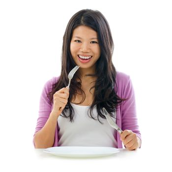 Beautiful Asian woman holding fork and knife with an empty plate ready for food, isolated on white background